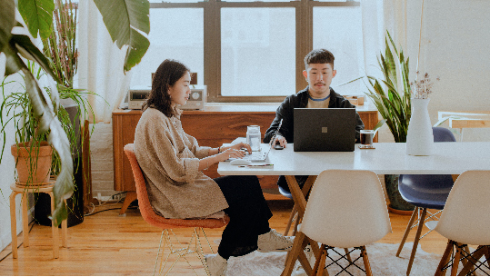 A young professional couple sits at their dining room table quietly working from home together.